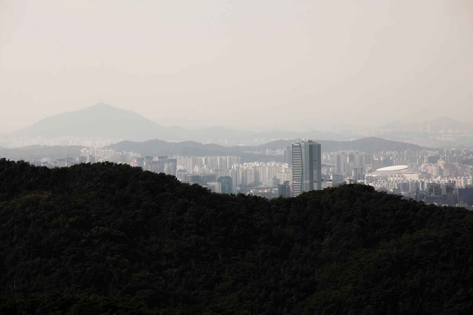 Aerial skyline of Seoul from forested hillsides, featuring distant mountains