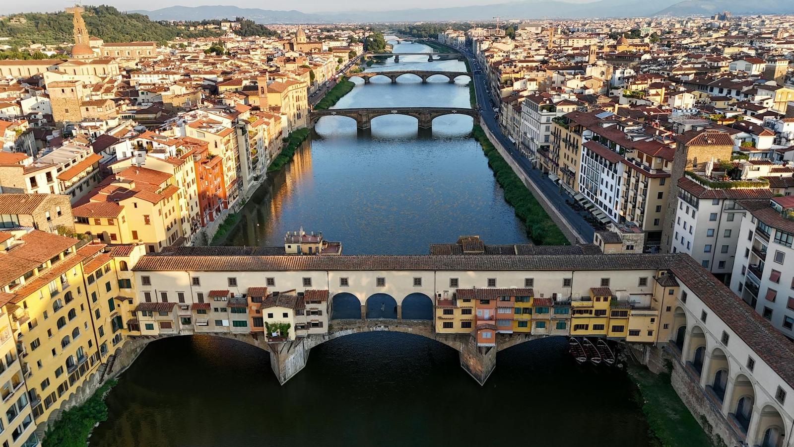 Aerial view of an arched shop-lined bridge spanning a river through a historic city