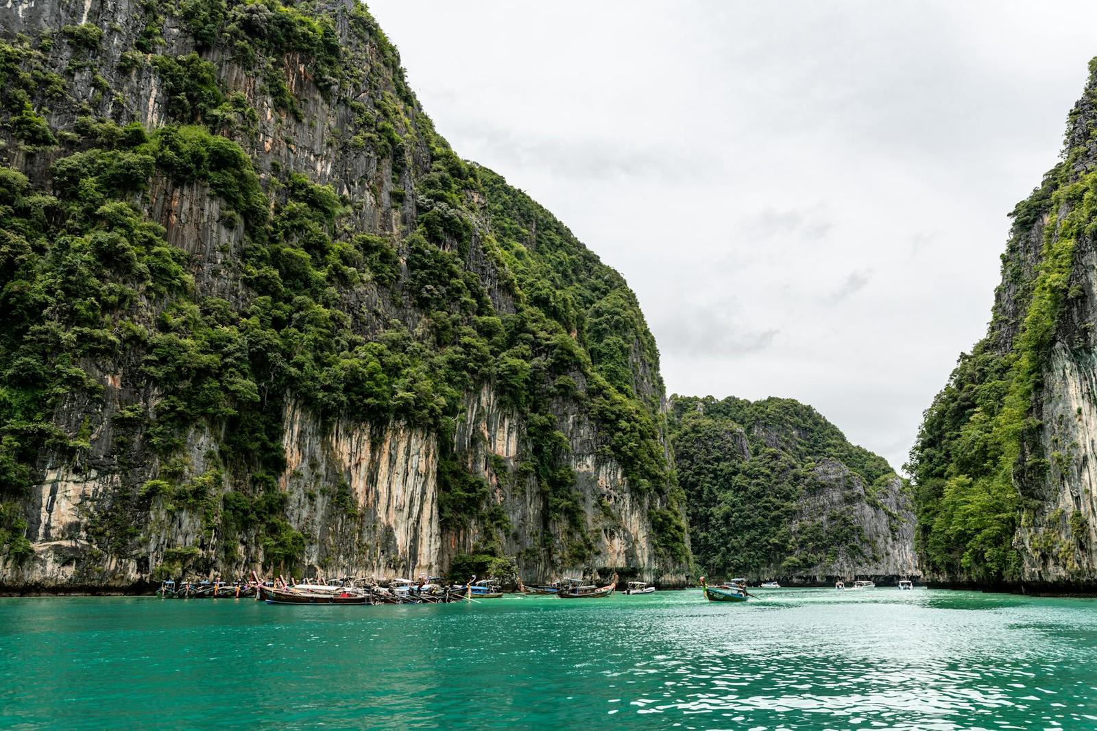 Boats passing through a narrow turquoise channel between sheer green cliffs