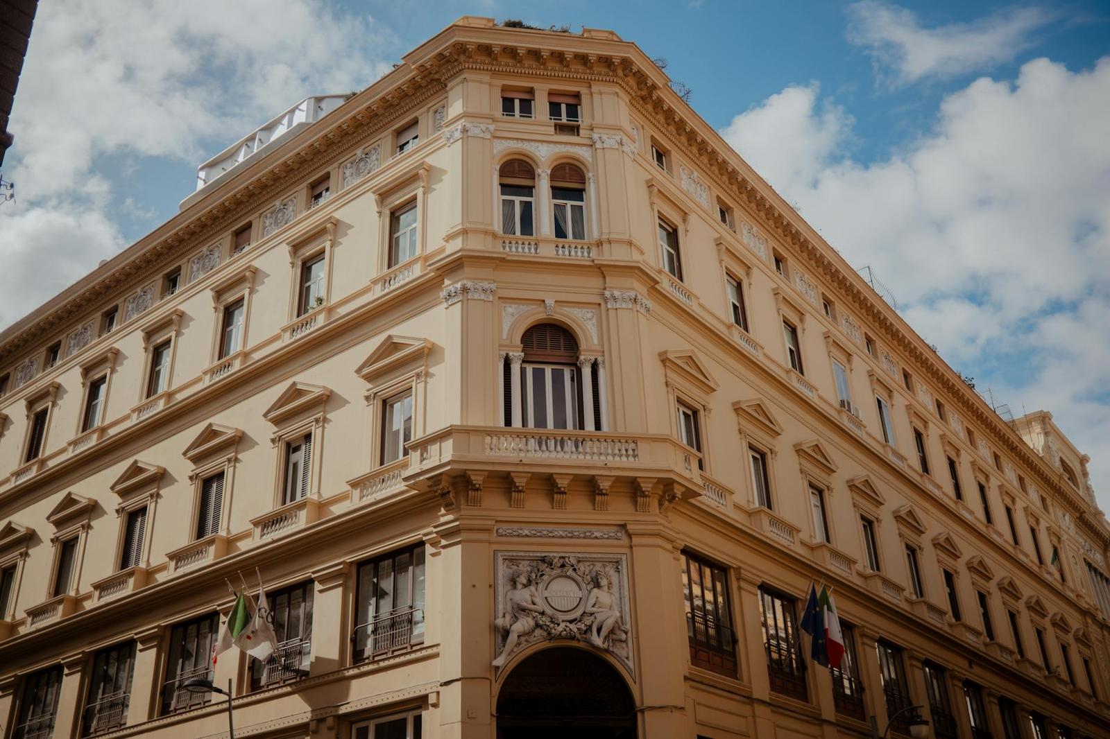 Cream corner building with an arched entrance and an Italian flag hanging beside it
