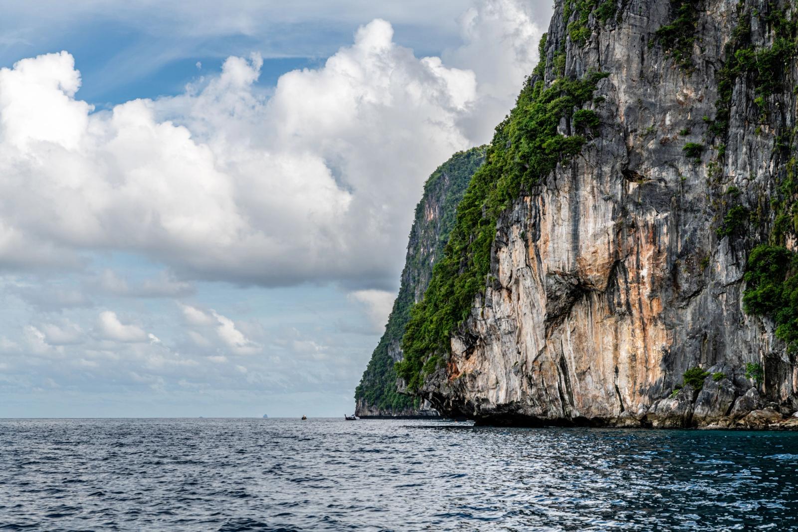 Stunning limestone cliffs rise over the vast ocean in Phuket, Thailand, under a cloud-filled sky