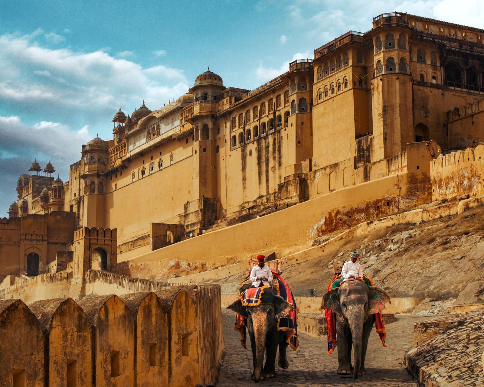 Riders atop elephants approaching a hilltop fort's sandstone ramparts