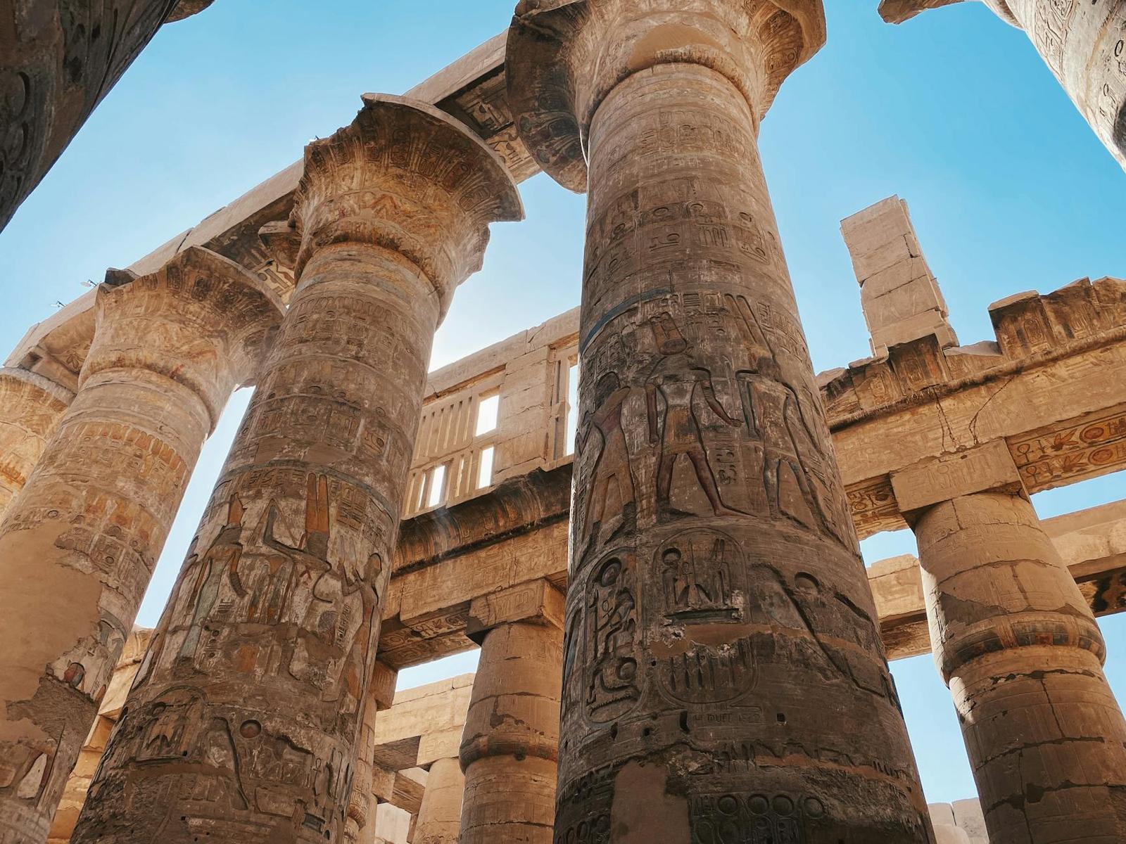 Massive carved stone columns of an ancient temple hall against a blue sky