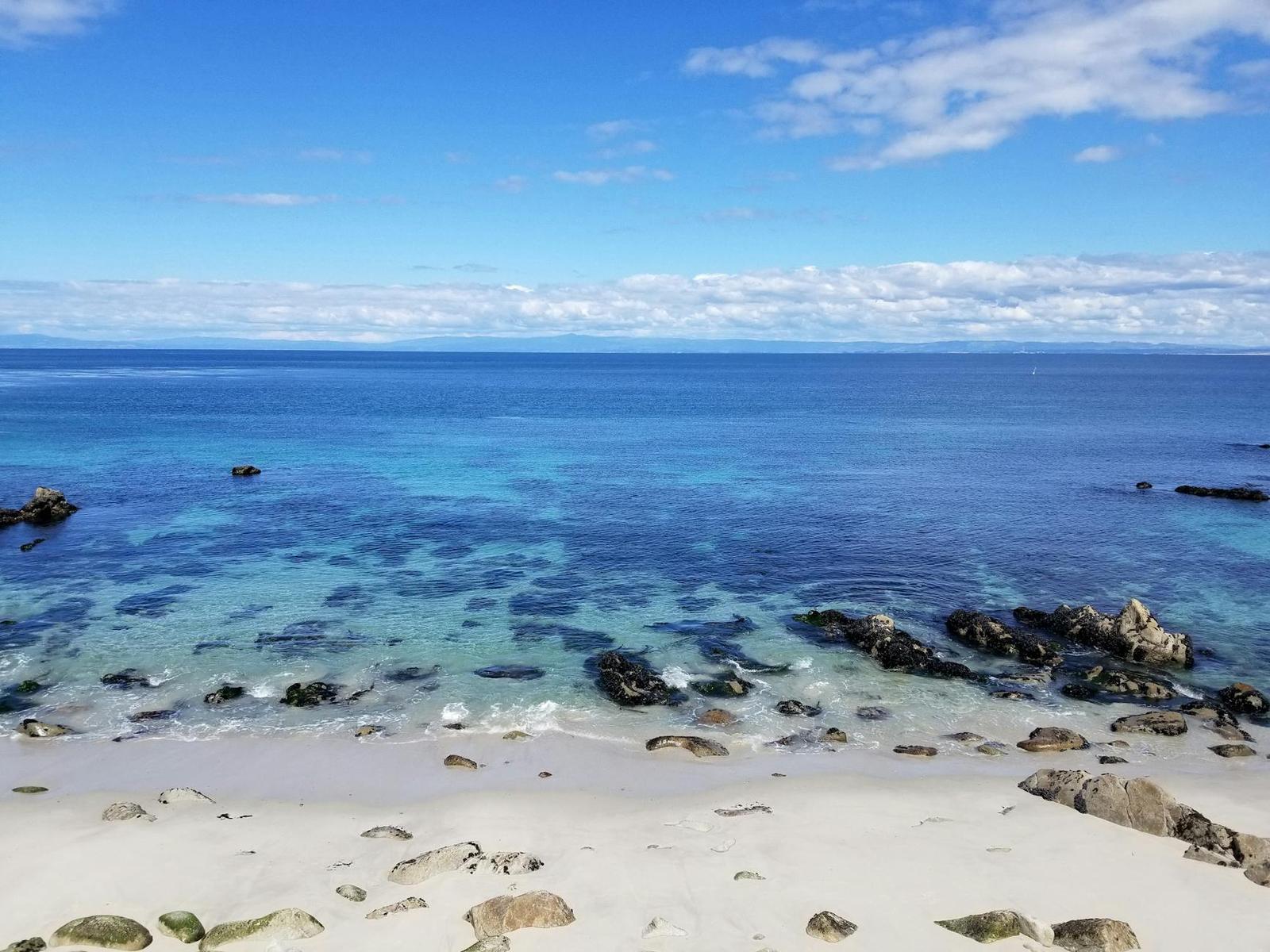 Clear turquoise water over rocks meeting a white sand beach under a blue sky