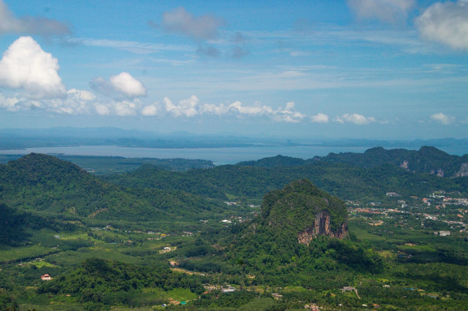 A high vantage over forested hills and karst peaks with the sea beyond
