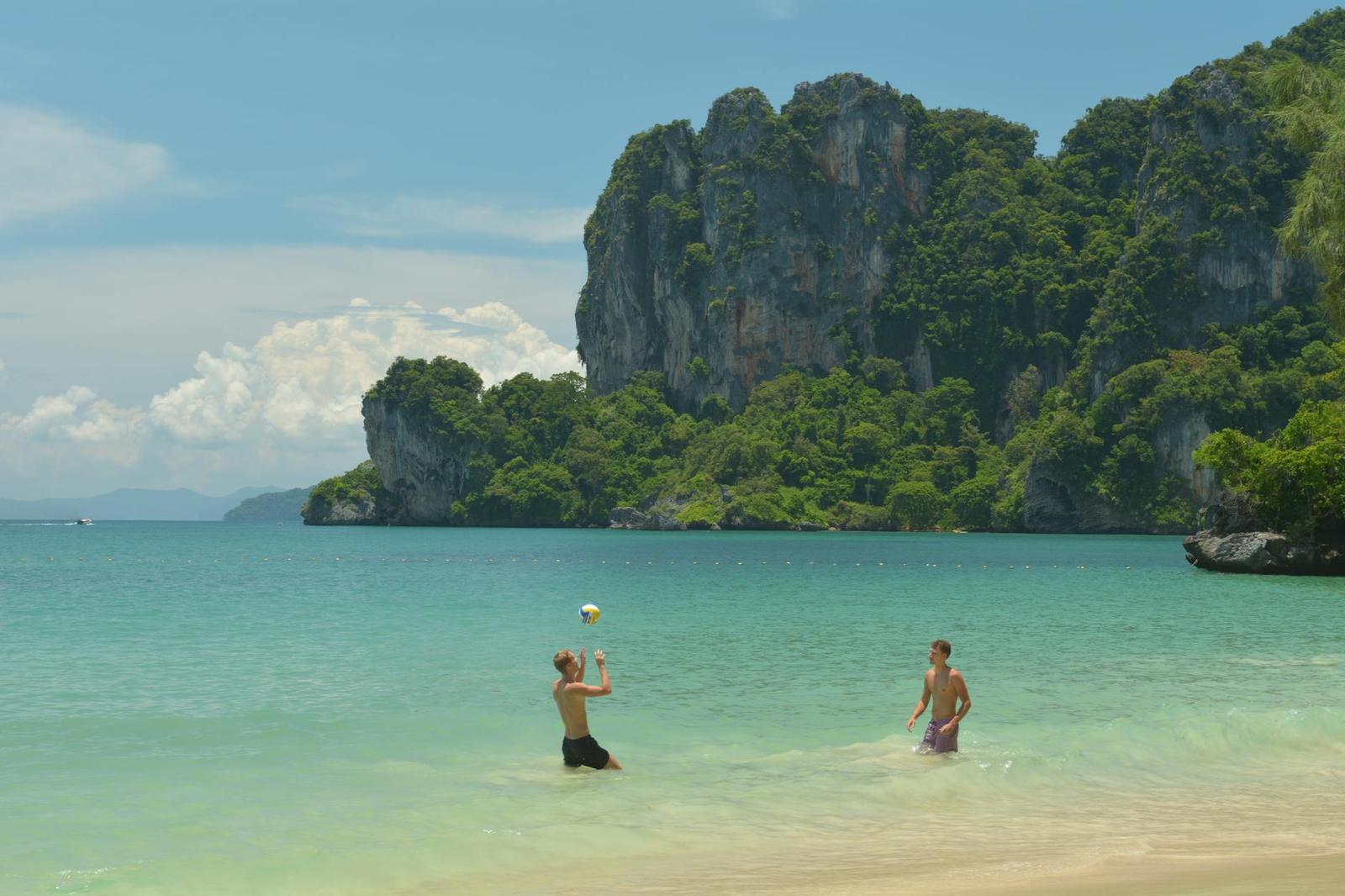 Two swimmers playing with a ball in a lagoon below limestone cliffs
