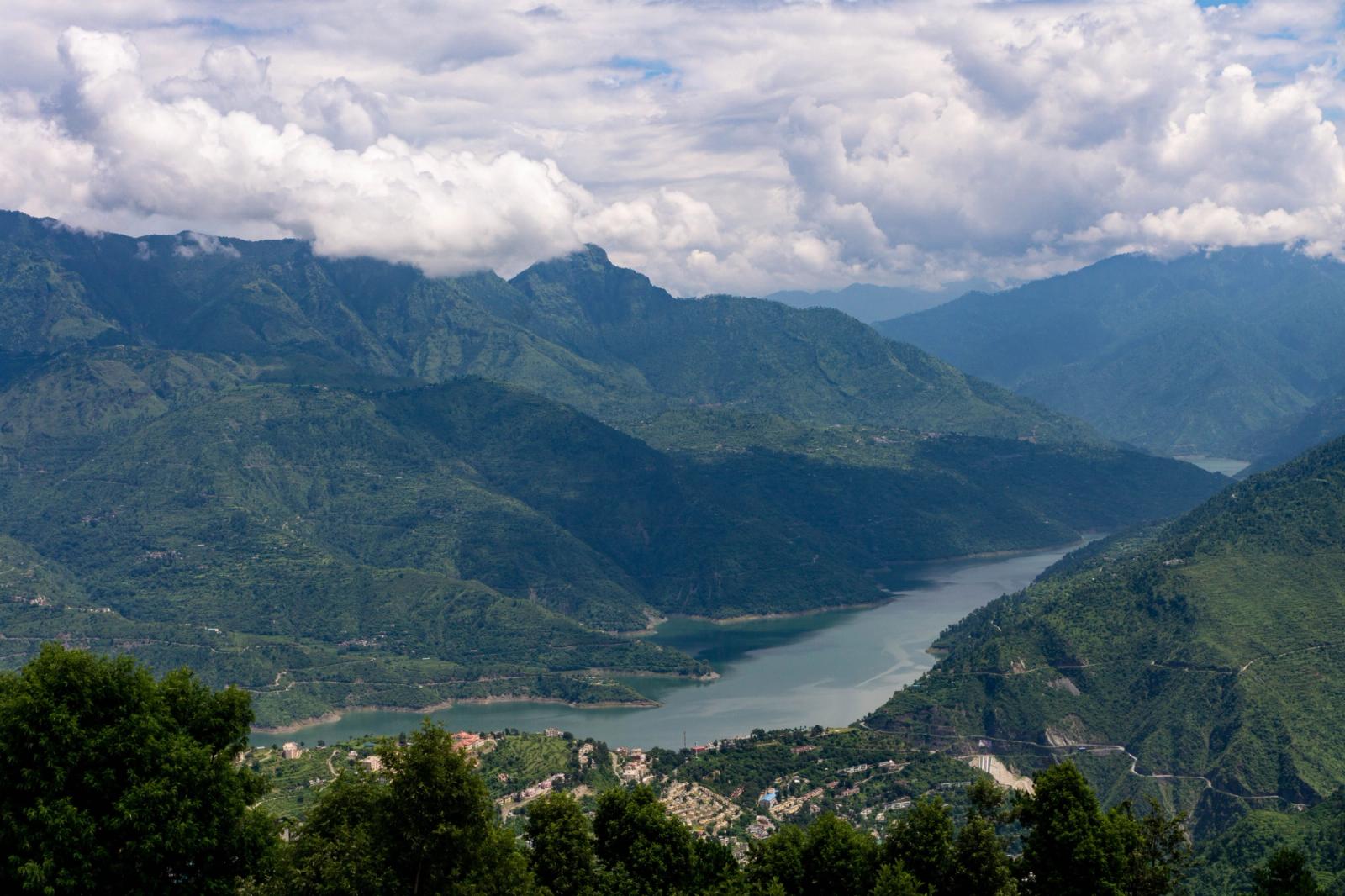 A breathtaking view of the New Tehri reservoir surrounded by lush green hills and cloudy skies in Uttarakhand, India