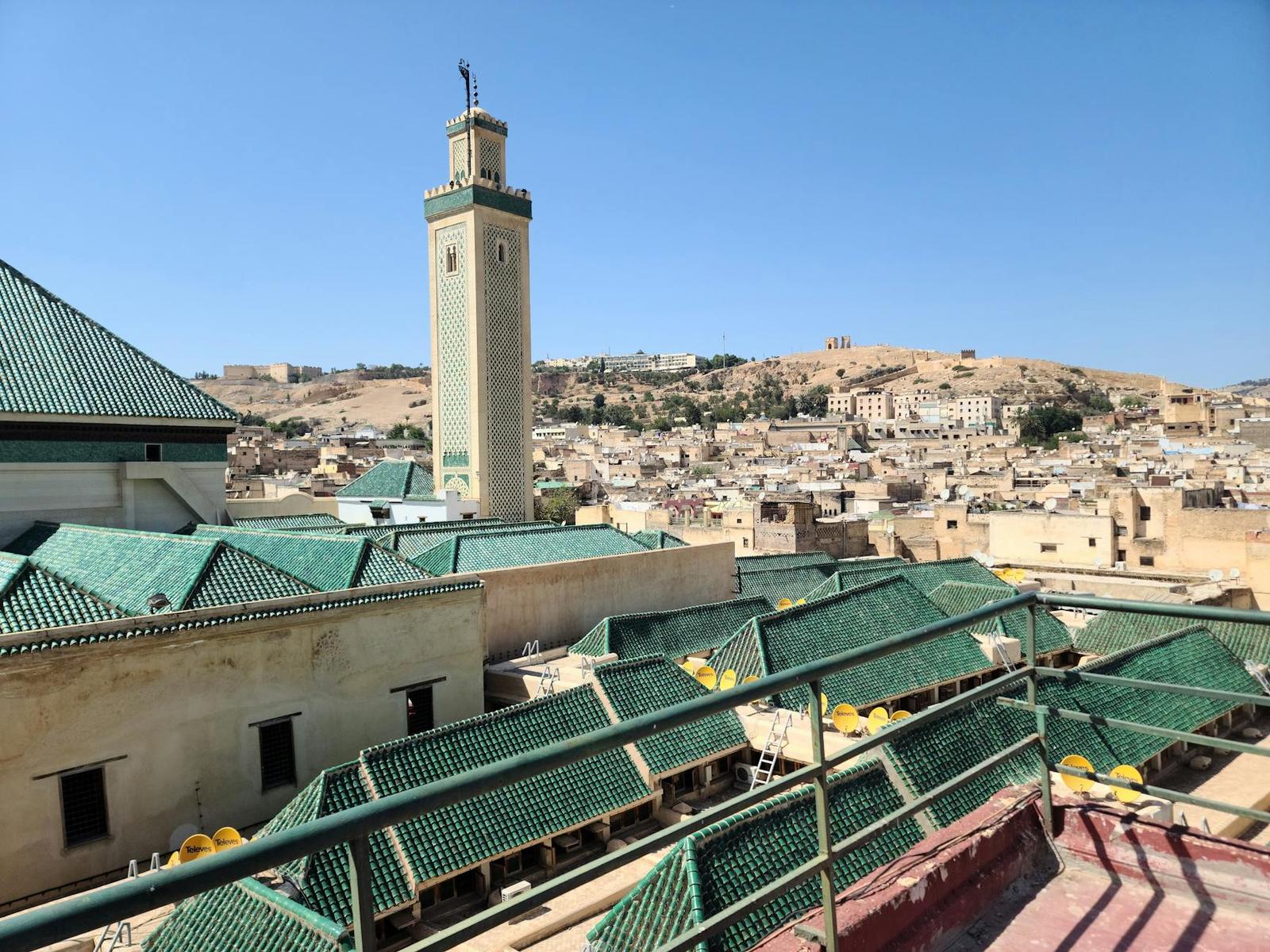 Green tiled rooftops and a tall minaret overlooking a hillside old town