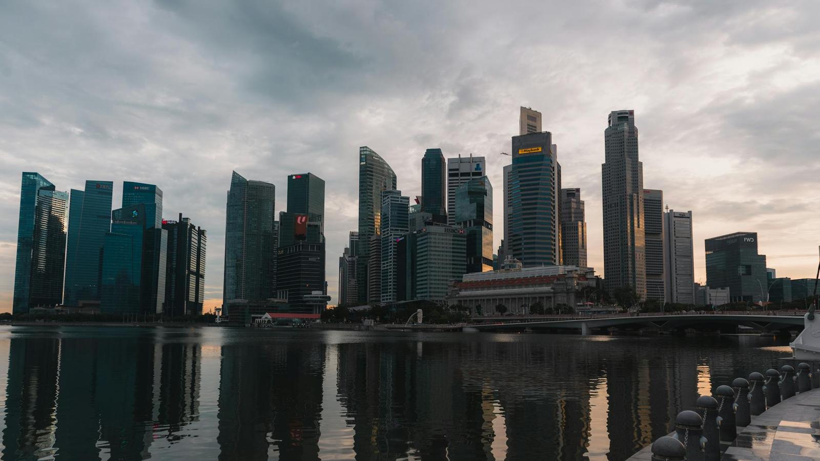 A city skyline of glass towers reflected in calm water at dusk