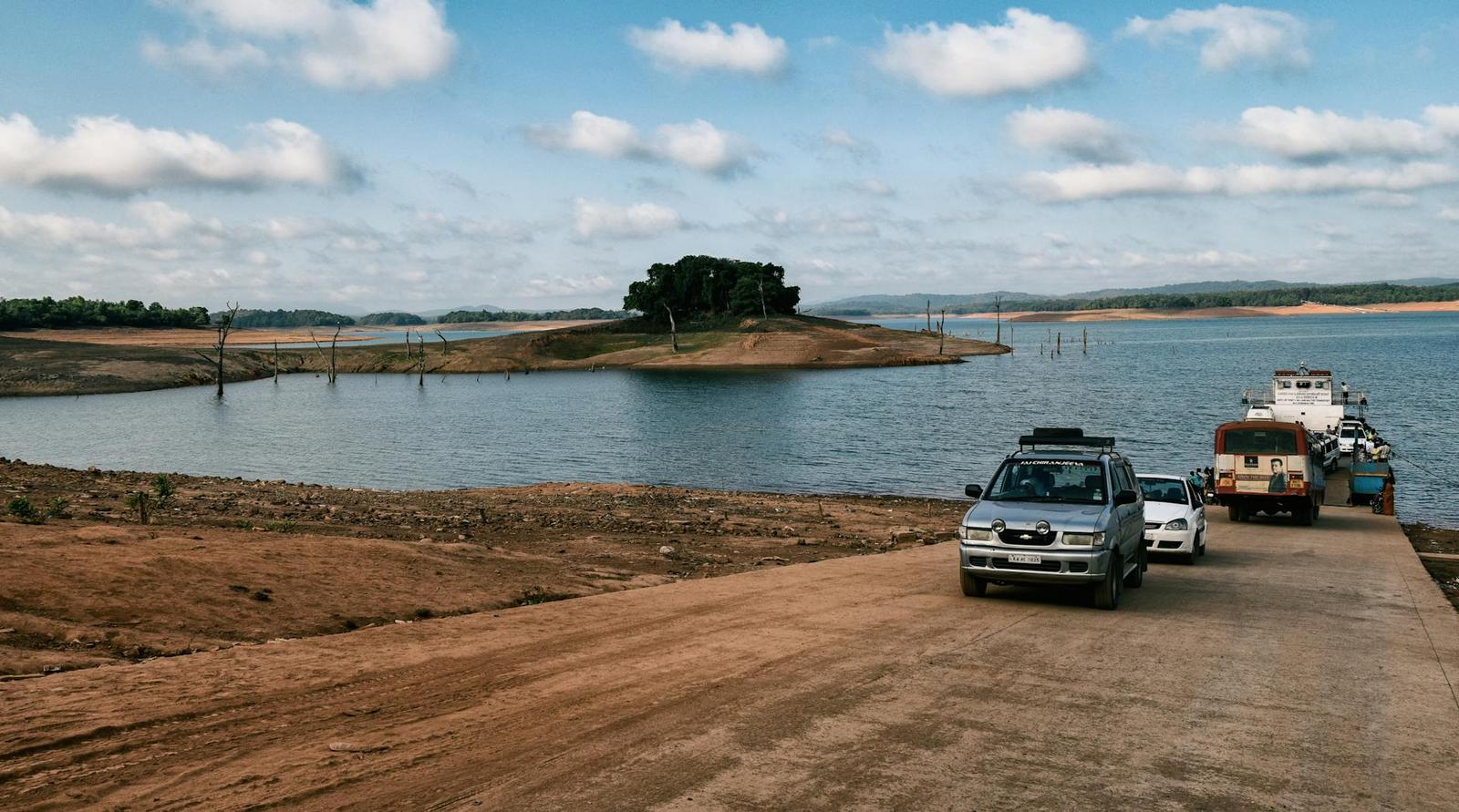 Vehicles parked beside a reservoir with a boat docked on the shore