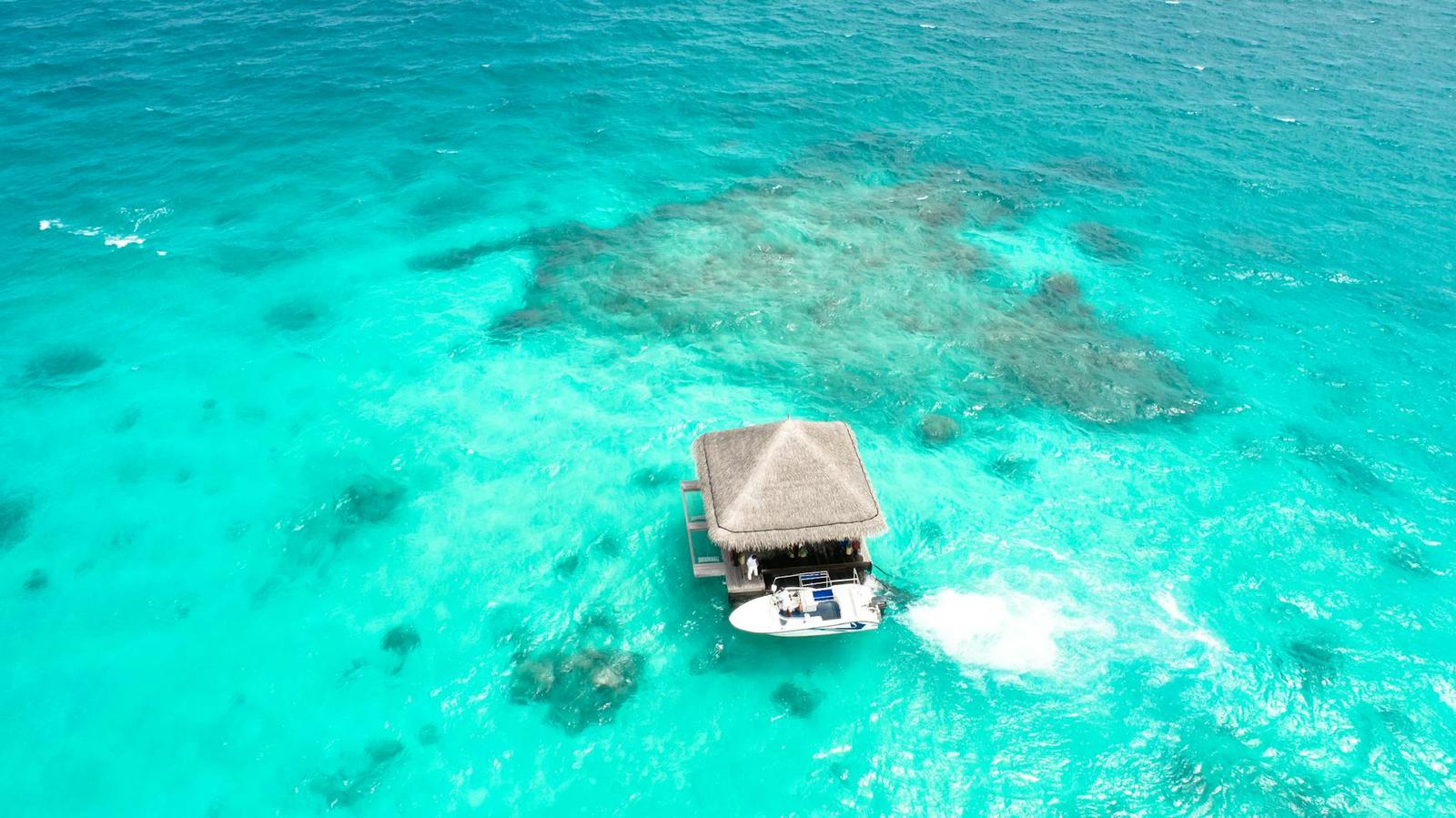 A speedboat pulling up to an overwater villa on a shallow reef