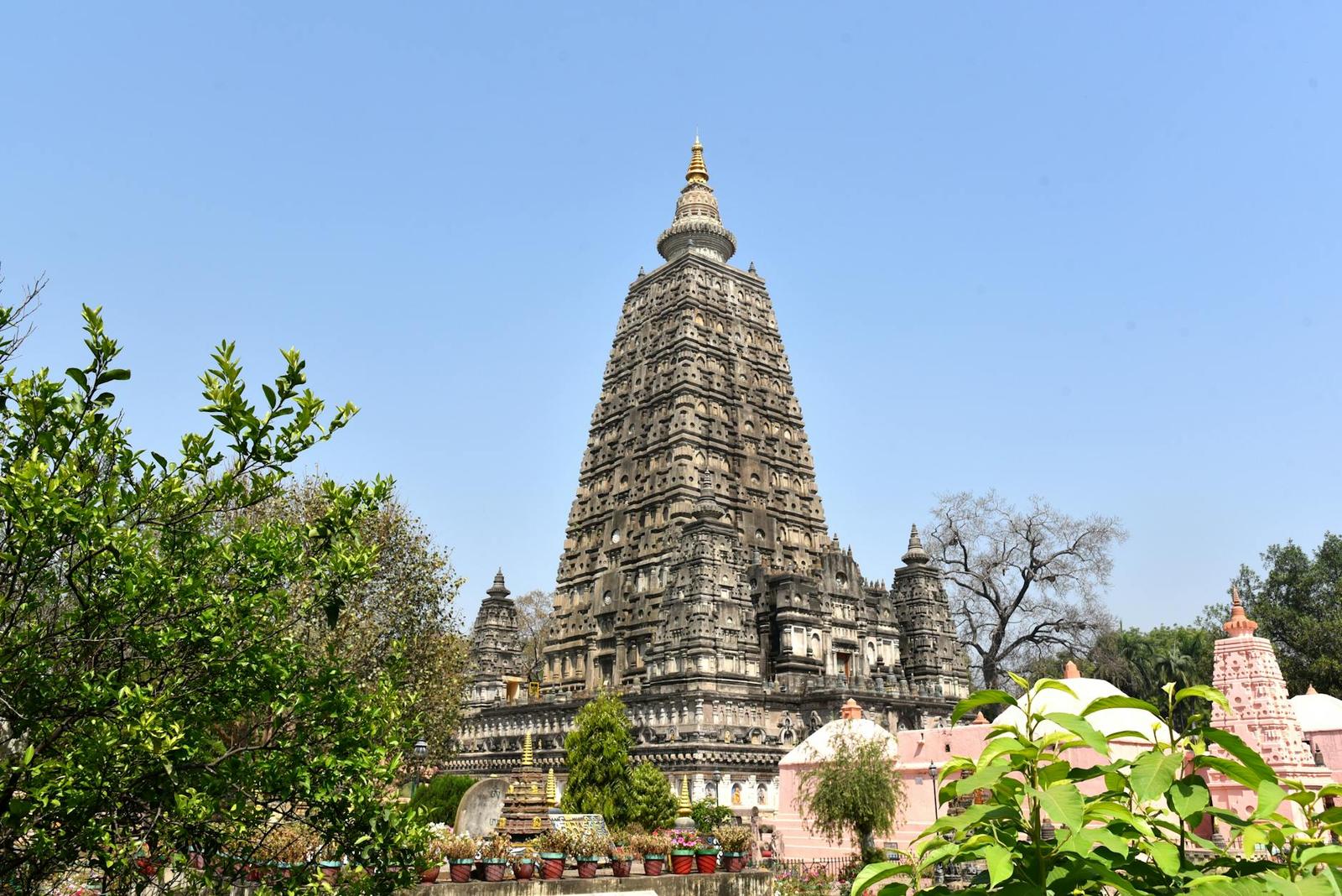 A tall stone temple spire with carved tiers rising above surrounding greenery