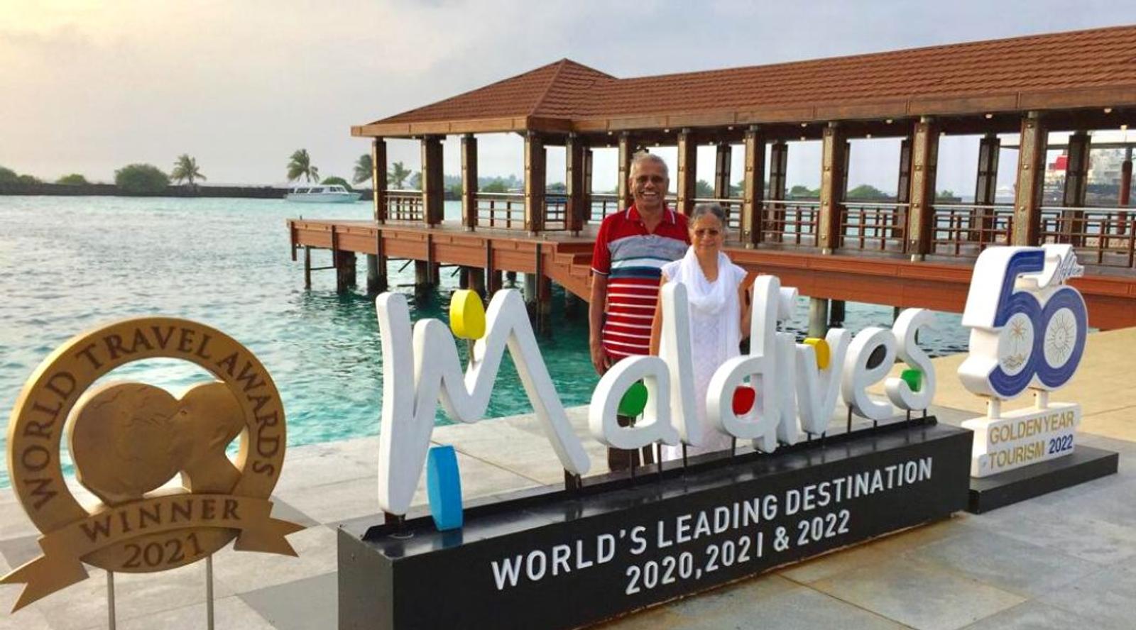 Two people posing in front of a 'Maldives' sign