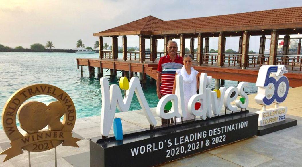 Two people posing in front of a 'Maldives' sign