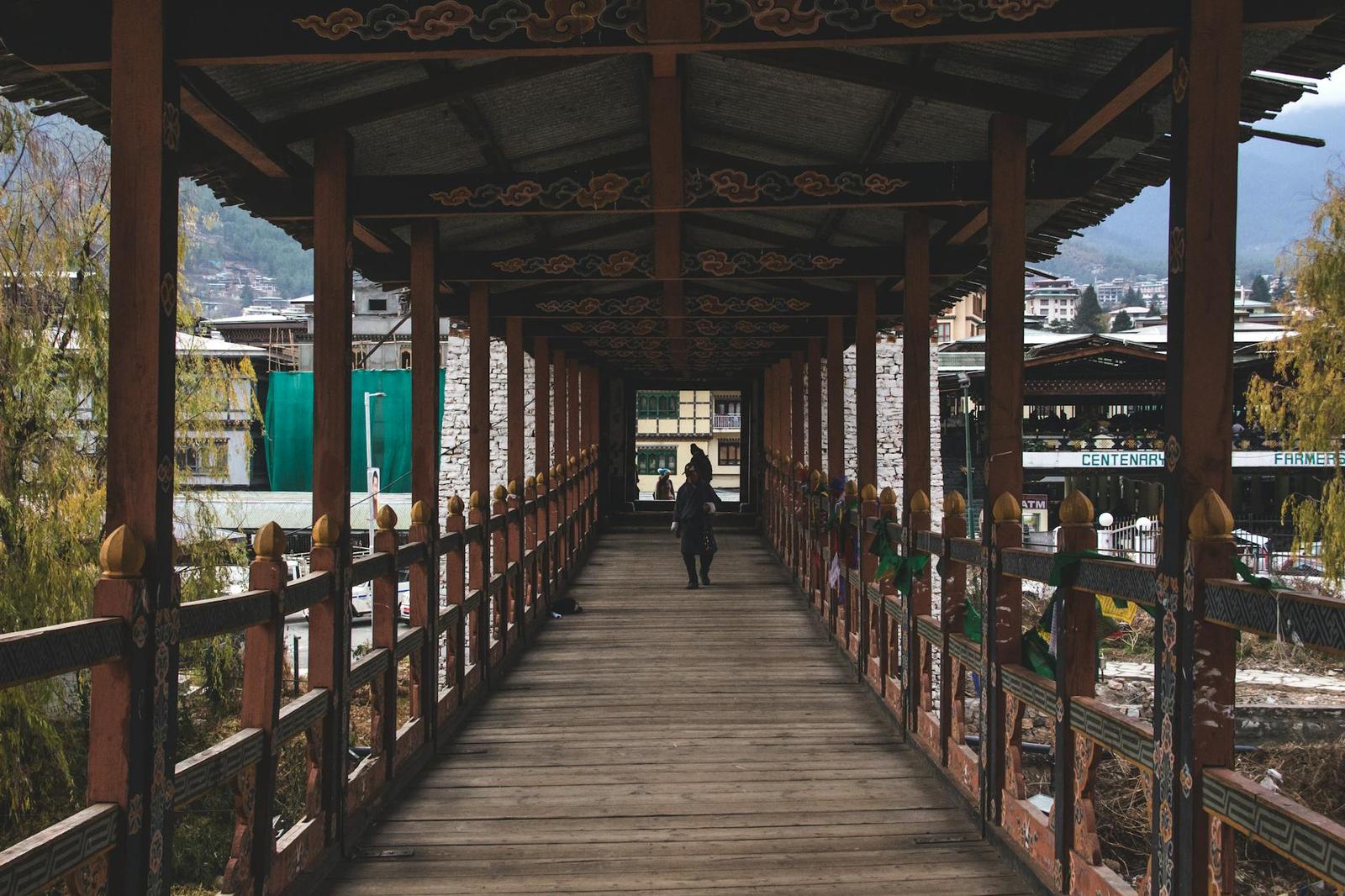 A figure walking through a covered wooden footbridge with painted beams