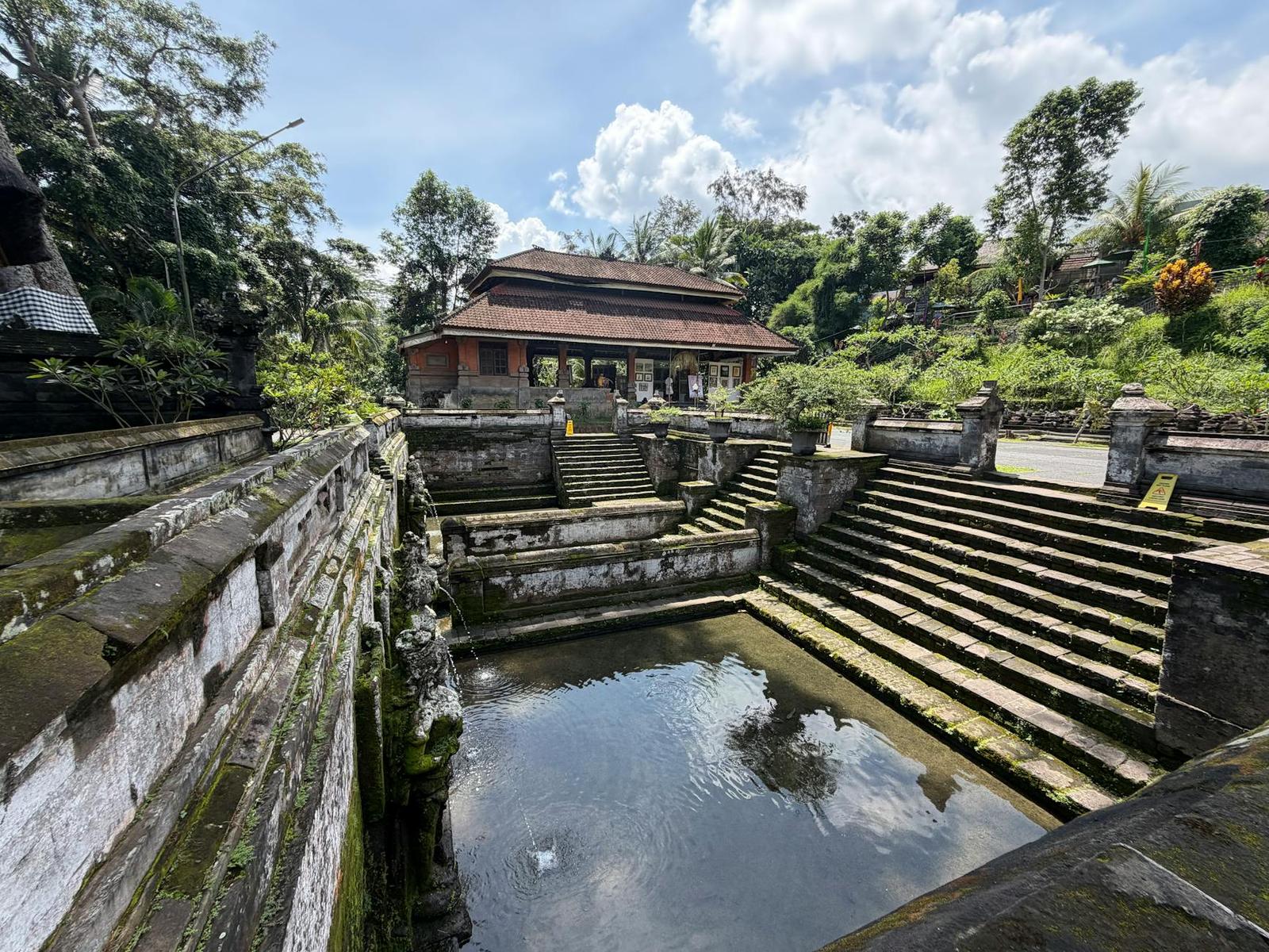 Moss-covered stone steps descend into a temple bathing pool beside a tiled pavilion