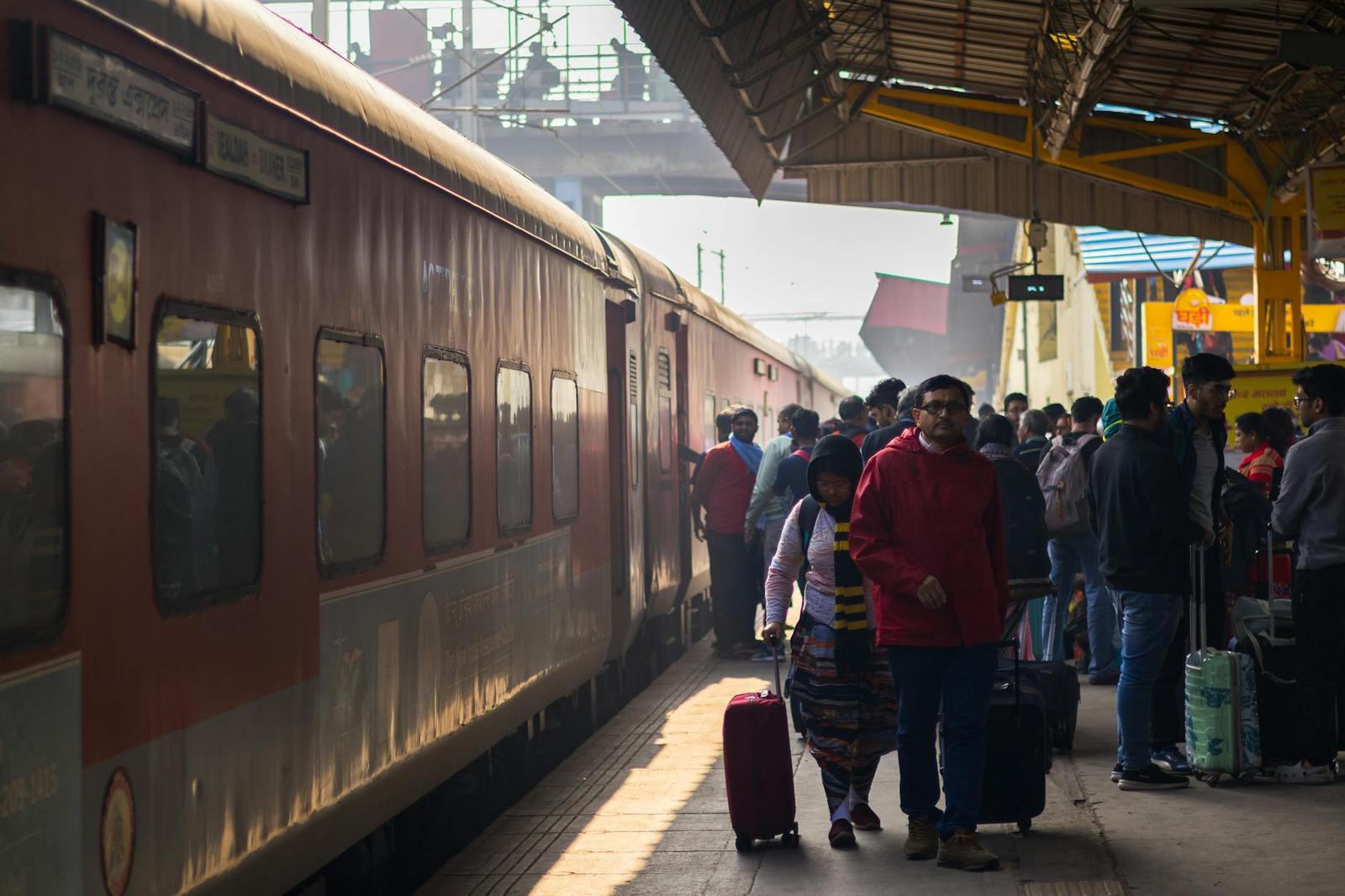 Passengers with rolling luggage walk along a train platform in morning haze