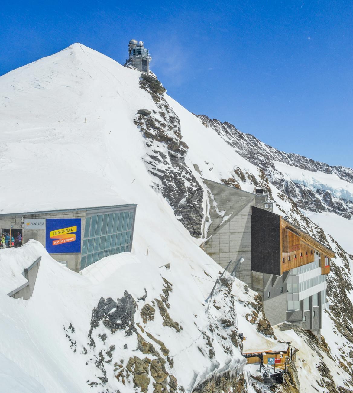 Picturesque view of buildings of ski resort on snowy mountain slope against clear blue sky
