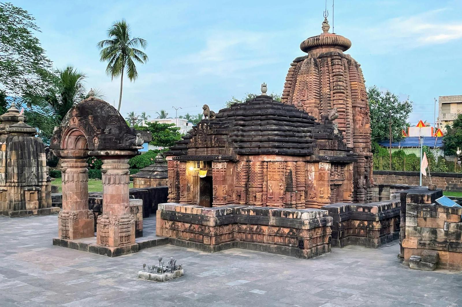 A stepped stone temple with a tall ridged tower beside a palm tree at dusk
