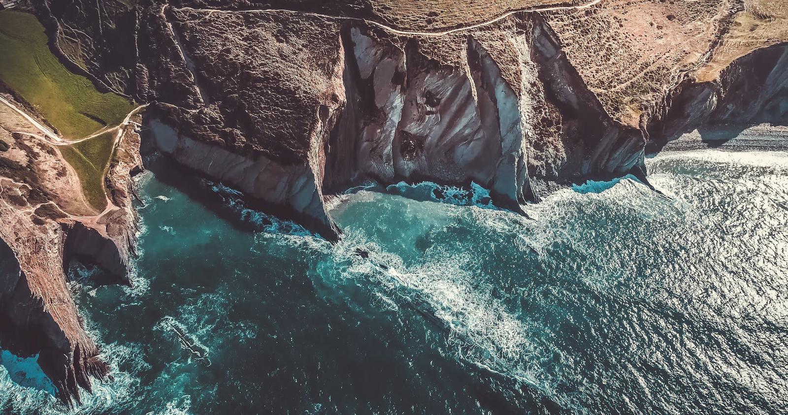 Aerial view of jagged sea cliffs with narrow inlets and turquoise water below