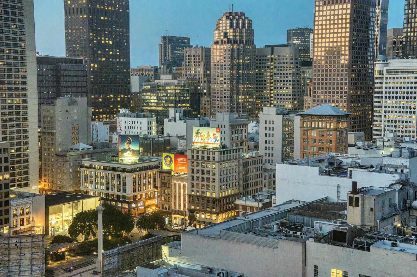 A downtown skyline at dusk with illuminated shopfronts and towers behind