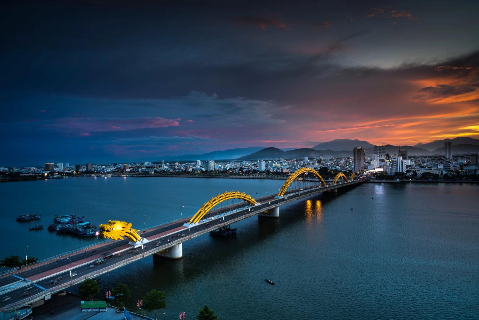 A stunning aerial view of the Dragon Bridge at sunset in Da Nang, Vietnam, highlighting illuminated cityscape