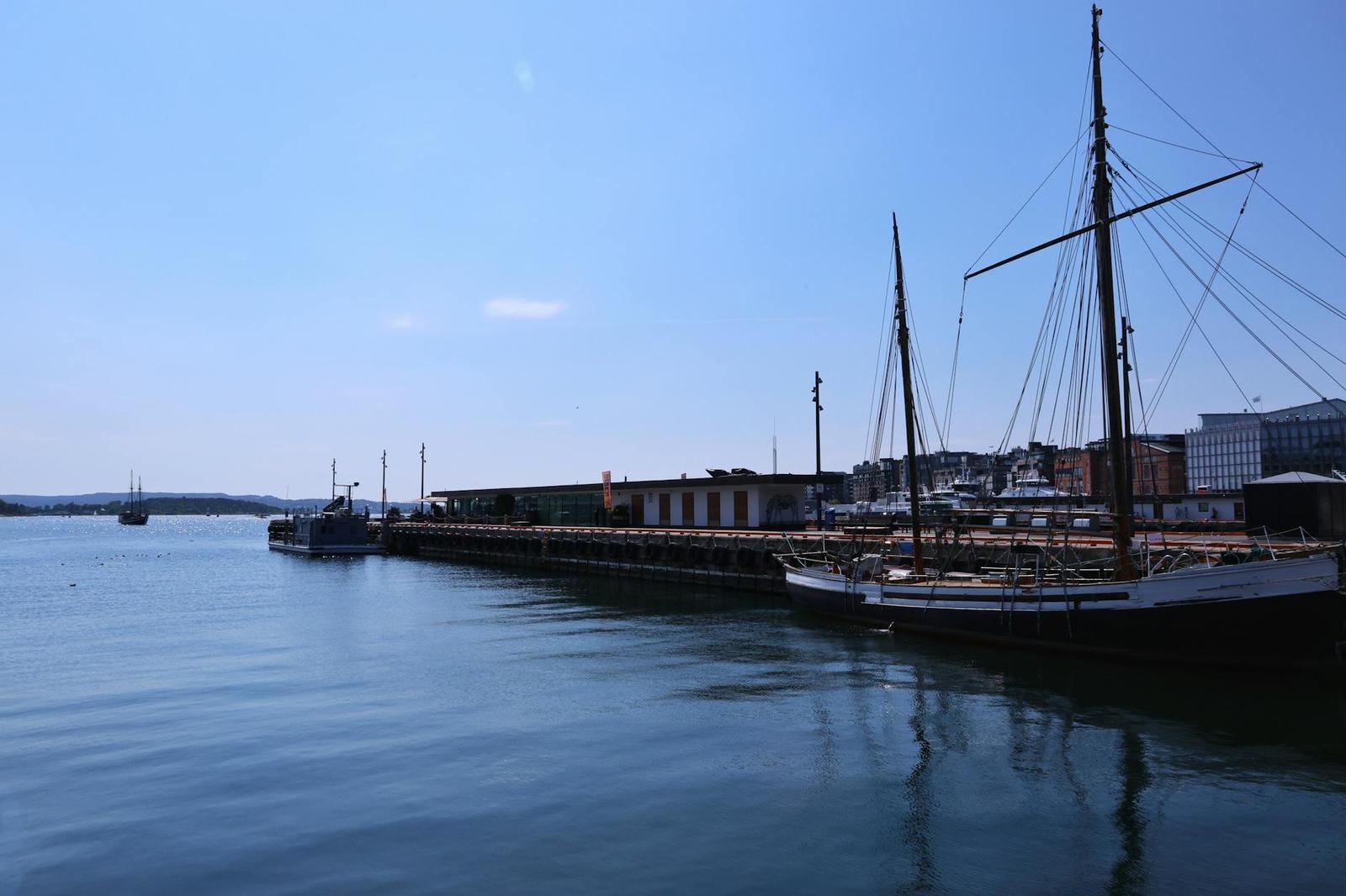 Tall-masted wooden sailing ship moored at a calm harbour pier