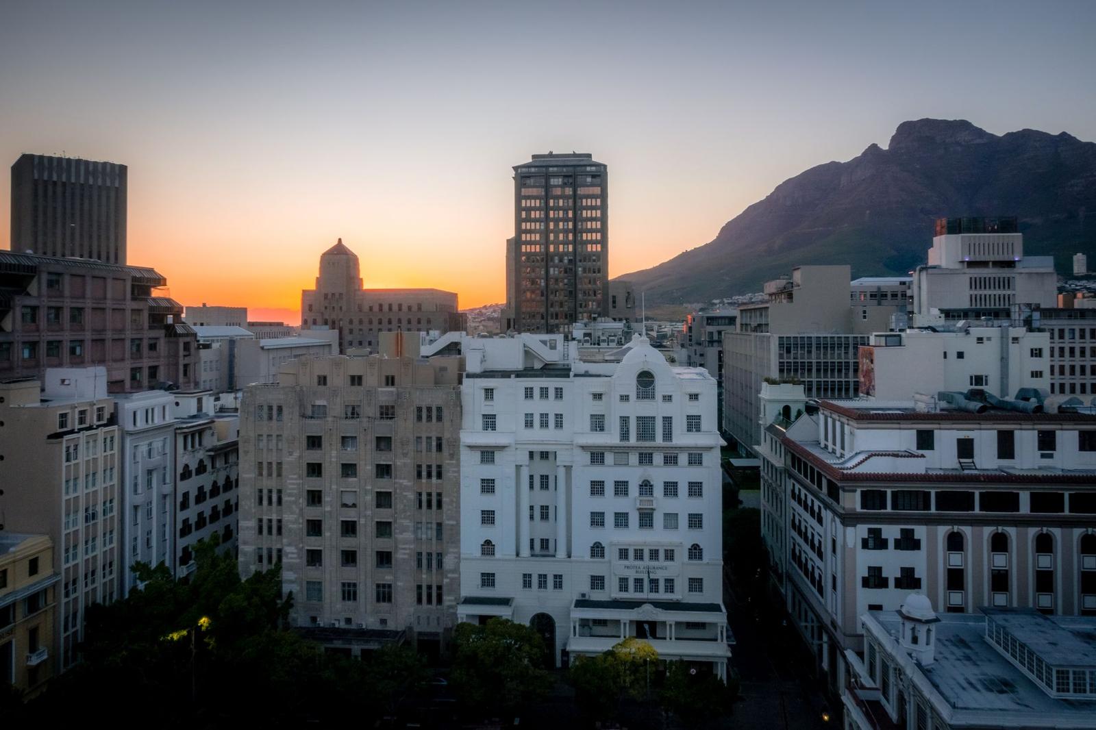 Historic city buildings glowing at sunset beneath a rugged mountain