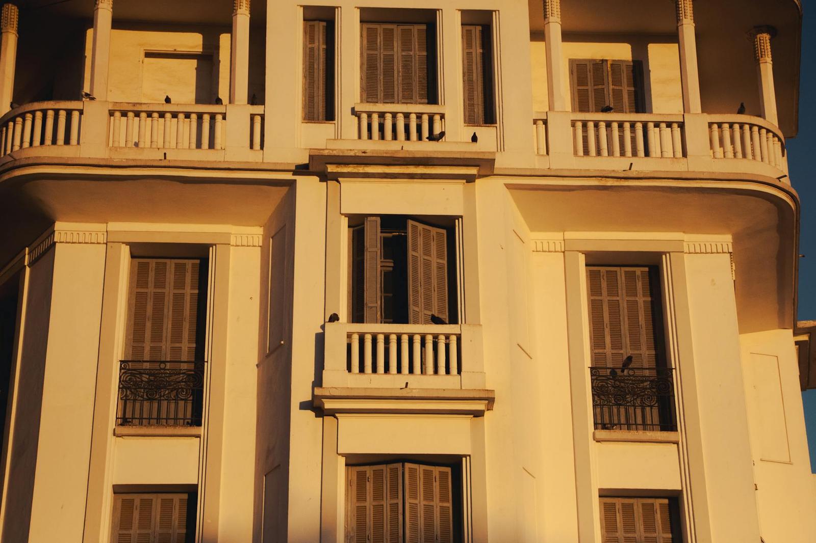 An ornate building facade with shuttered windows and balconies lit at golden hour