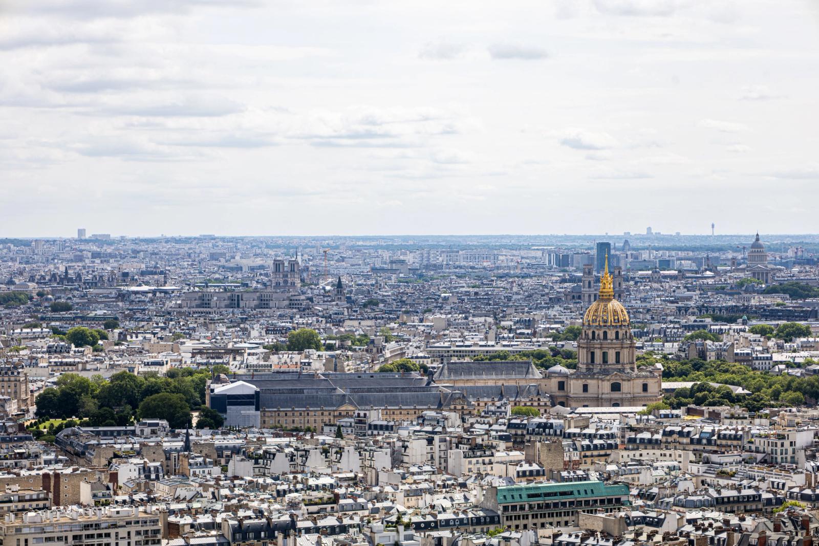 Sweeping aerial view of Paris skyline featuring the iconic Les Invalides dome under cloudy skies