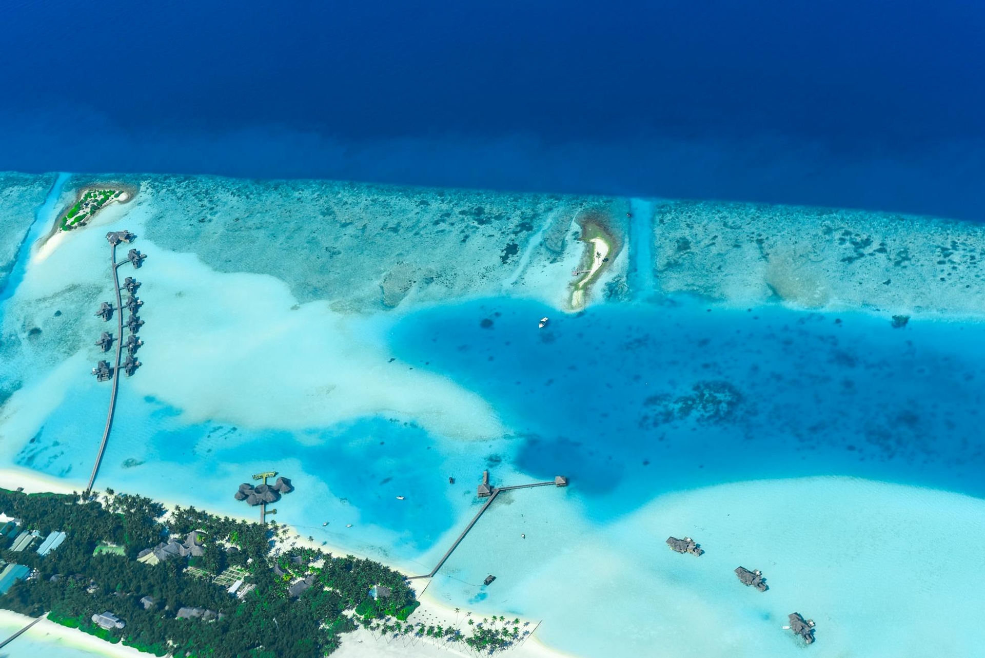 Aerial view of overwater villas fringing a shallow lagoon resort