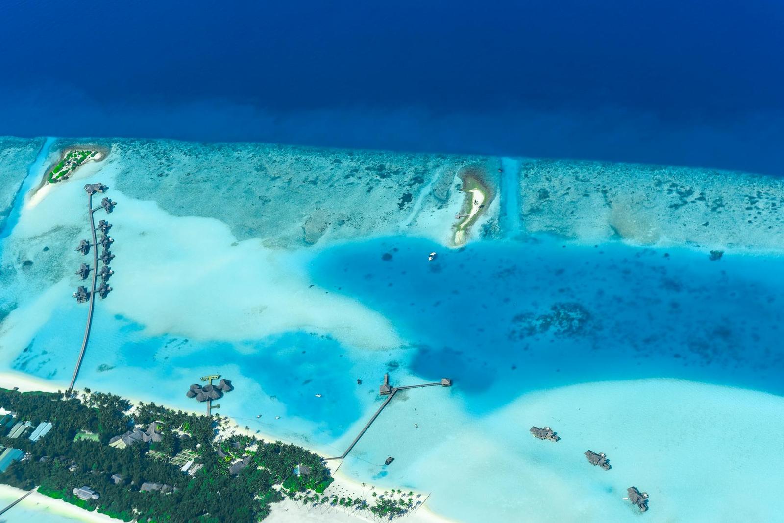 Aerial view of overwater villas fringing a shallow lagoon resort