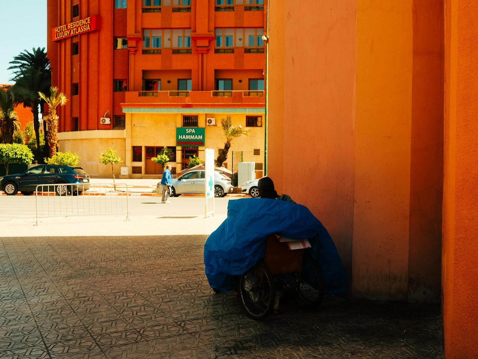 A tarp-covered cart parked in shade beside an orange hotel facade