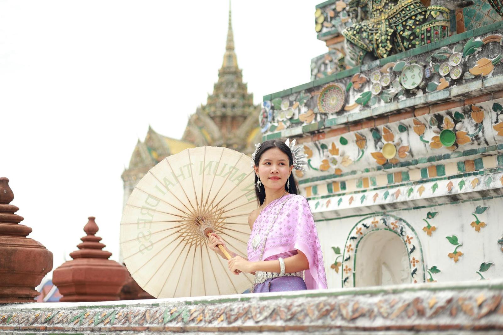 A woman in a lilac traditional dress holds a parasol beside an ornately tiled temple spire