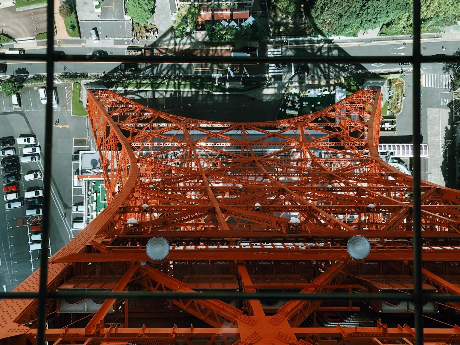 Looking down through the orange latticework of a tower to the street below