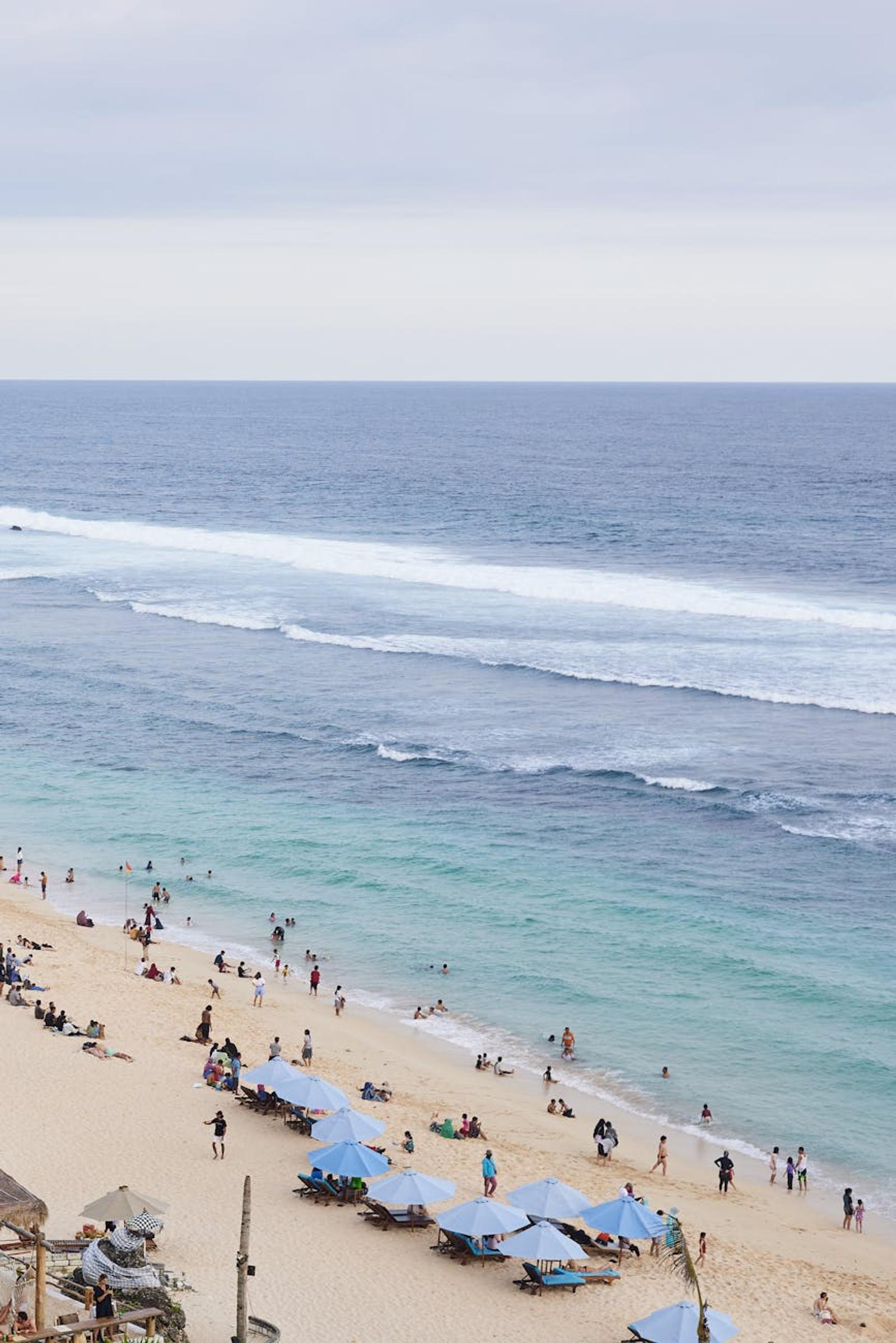 A vibrant beach in Bali, Indonesia with tourists enjoying under blue umbrellas