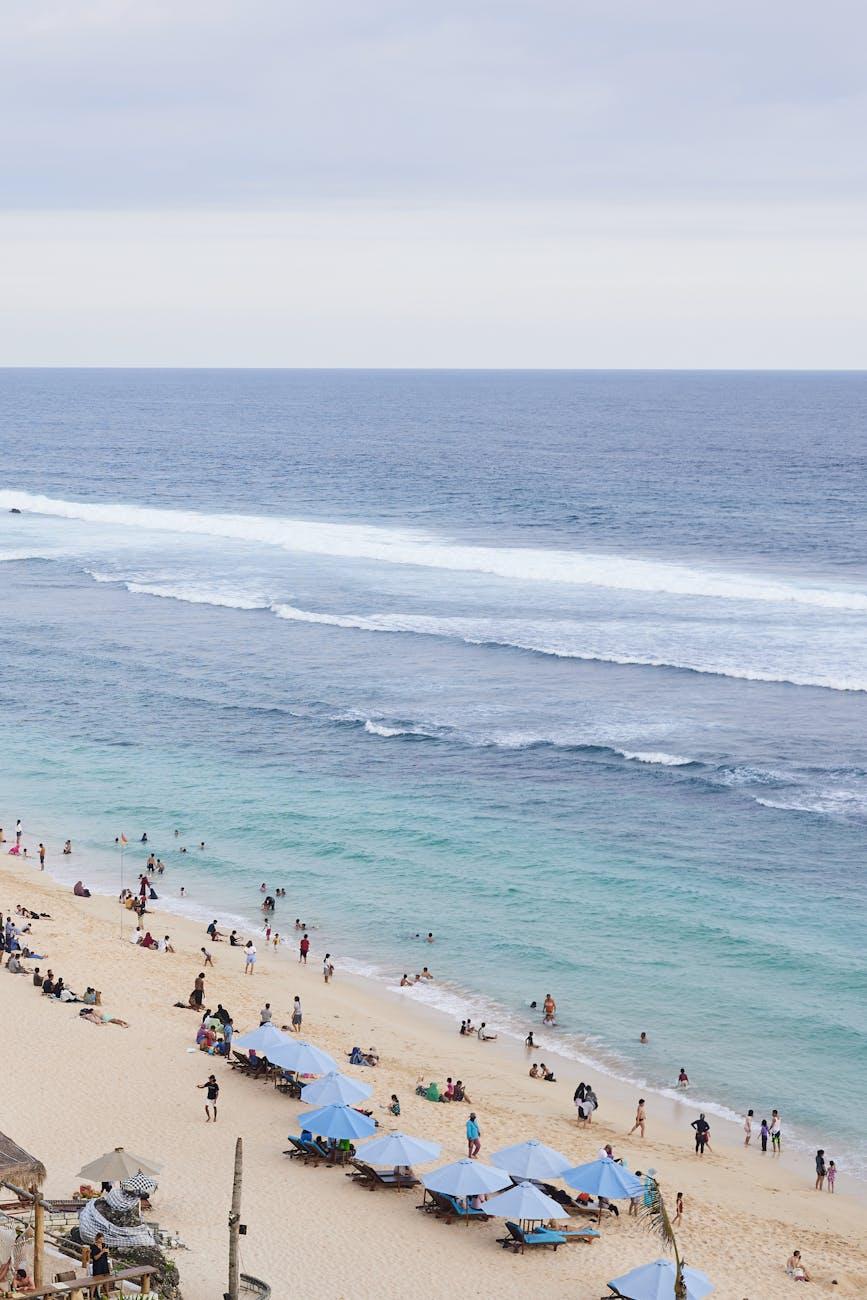 A vibrant beach in Bali, Indonesia with tourists enjoying under blue umbrellas