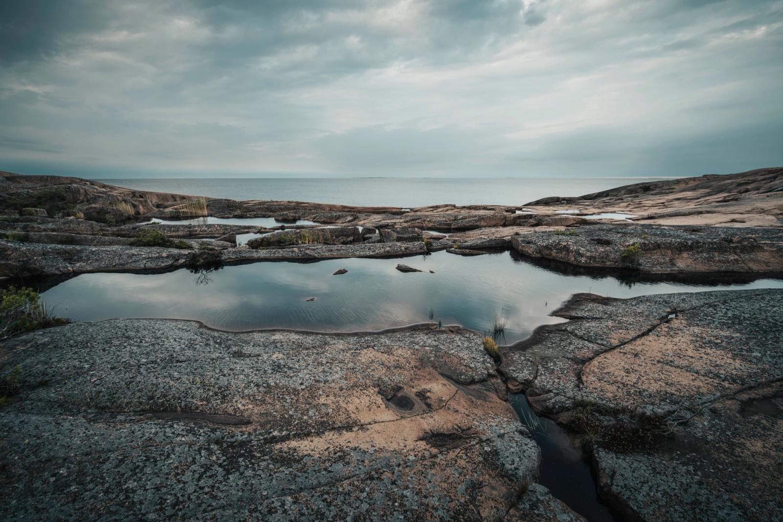 A tranquil rocky coastal scene with reflective pools under a cloudy sky