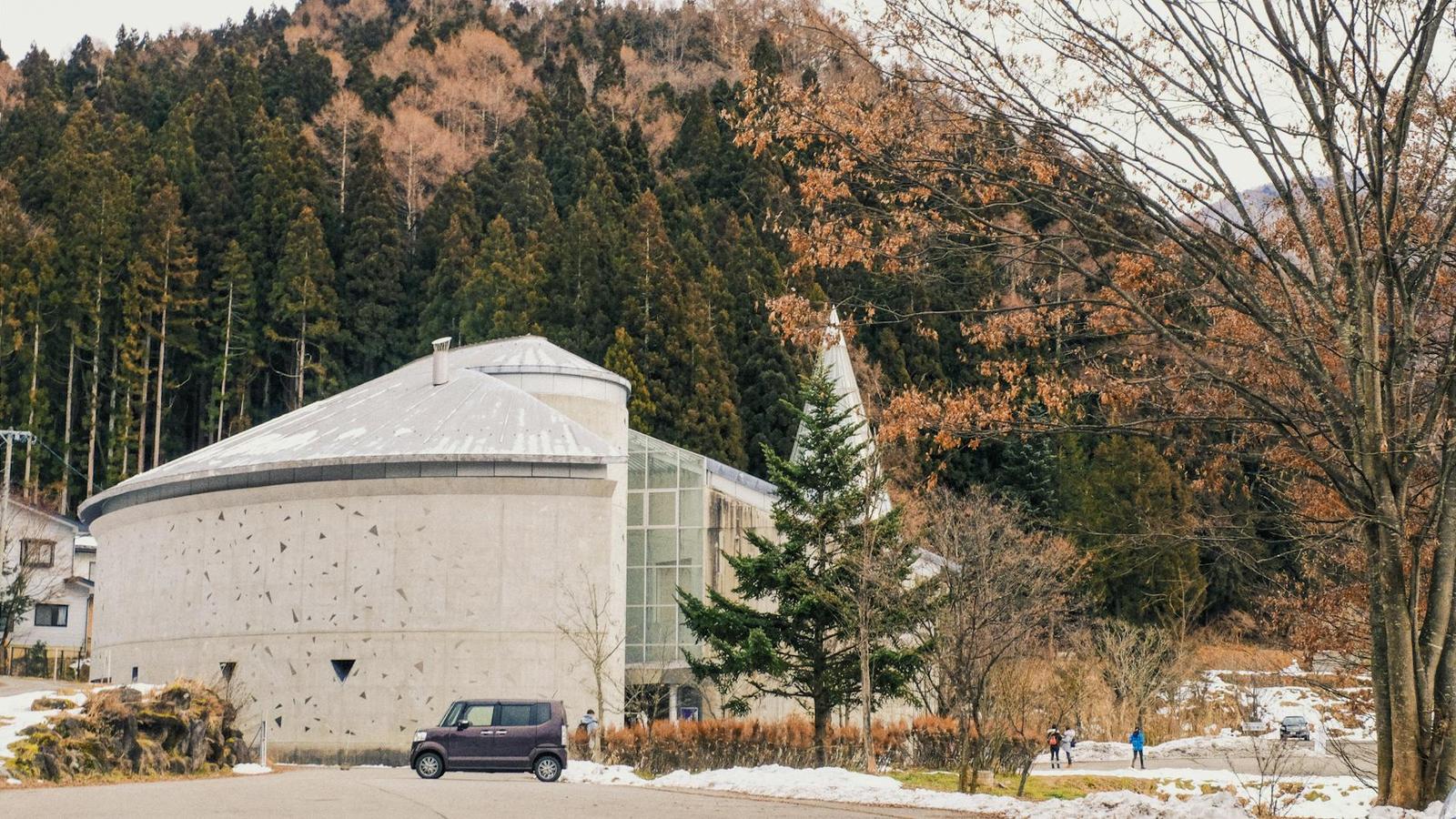 A round concrete and glass building set against a forested mountainside