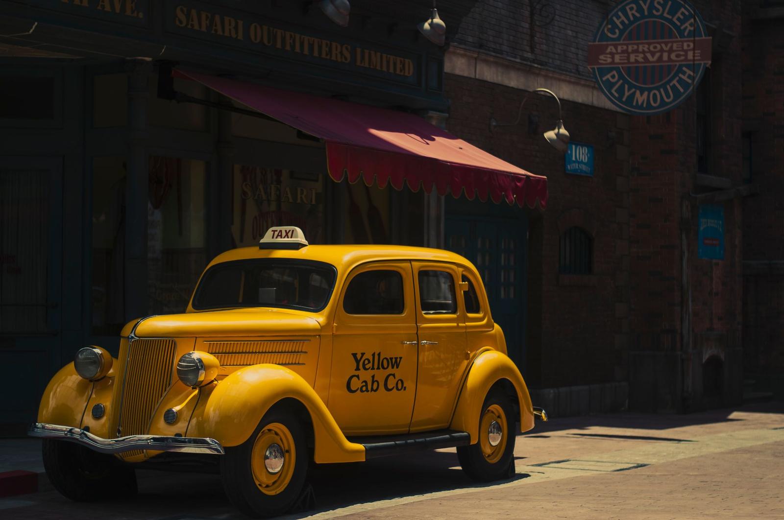 A vintage yellow taxi cab parked outside a themed street set with striped awnings