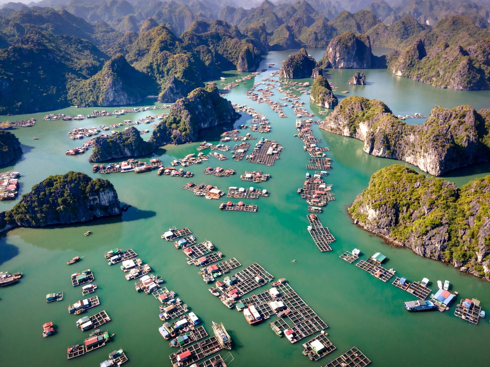 Aerial view of floating villages amidst limestone islands in a vibrant bay