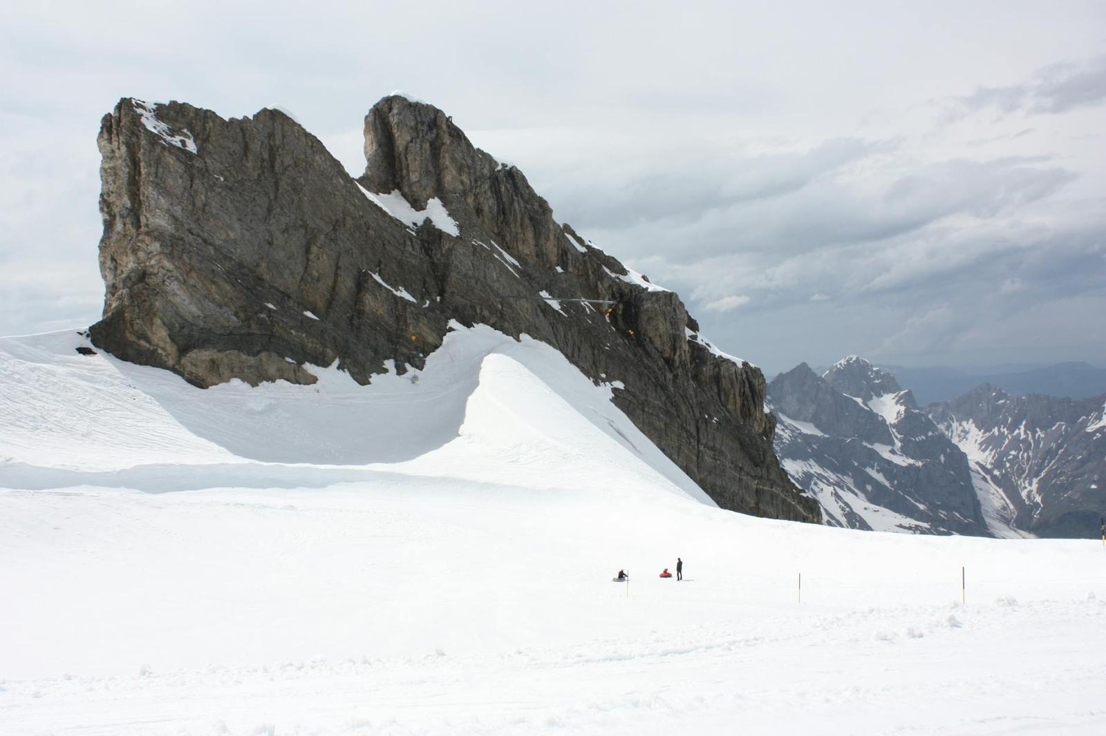 Jagged rock outcrop rising from a snowfield with distant figures walking below
