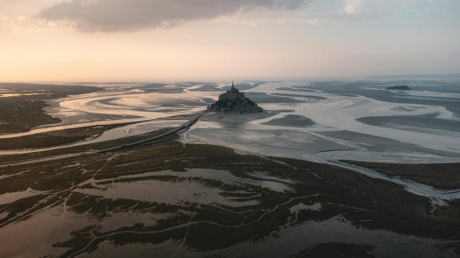 A fortified island abbey rising from a vast tidal flat at dusk