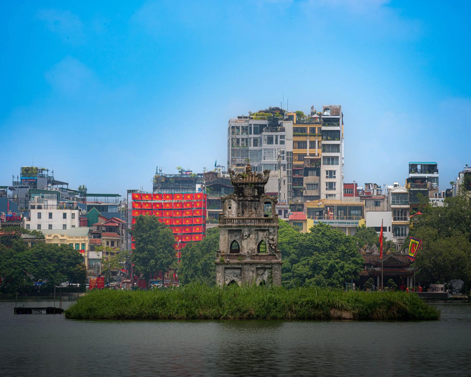 Turtle Tower standing prominently in Hoan Kiem Lake, Hanoi, with cityscape background under a bright sky