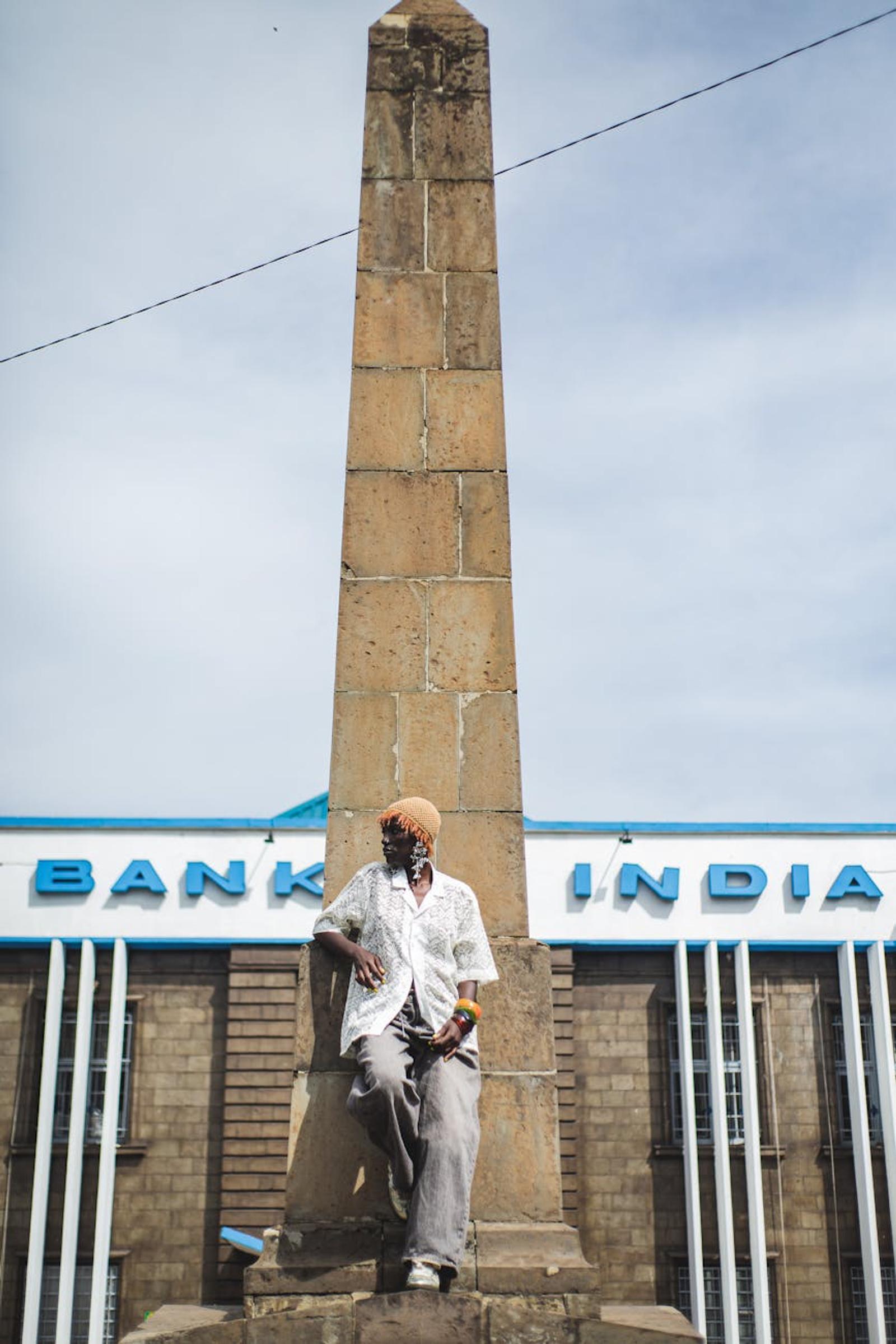 A man leaning against a tall stone obelisk outside a bank facade