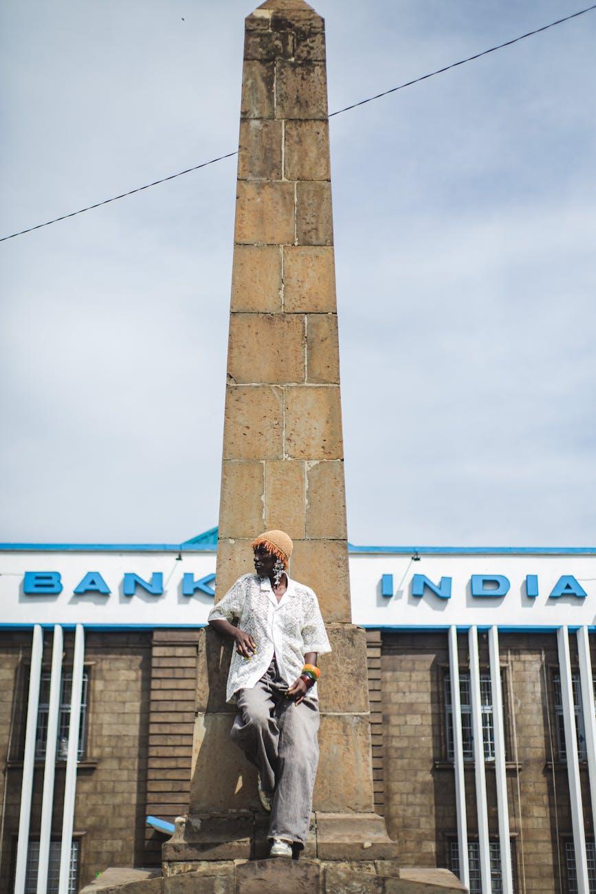 A man leaning against a tall stone obelisk outside a bank facade