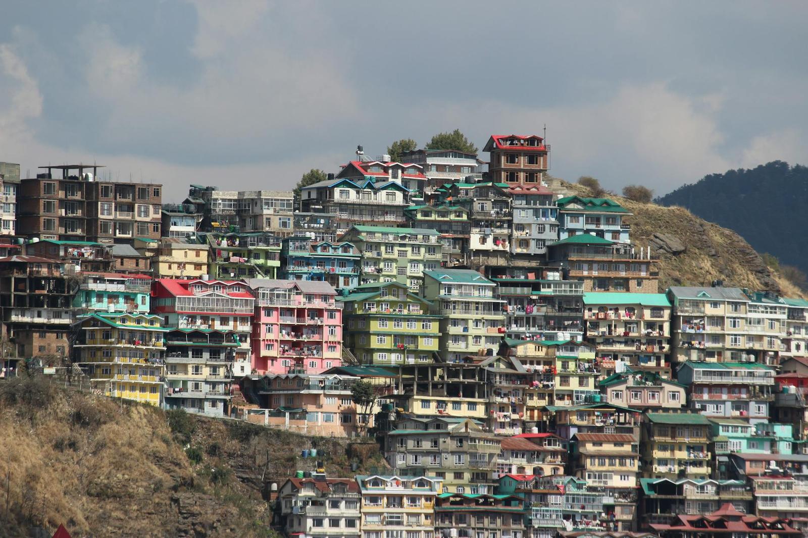 Densely packed multicoloured houses covering a steep hillside under a cloudy sky
