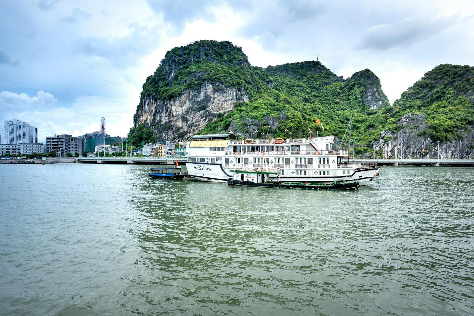 Idyllic boats in Halong Bay with limestone cliffs and cityscape backdrop