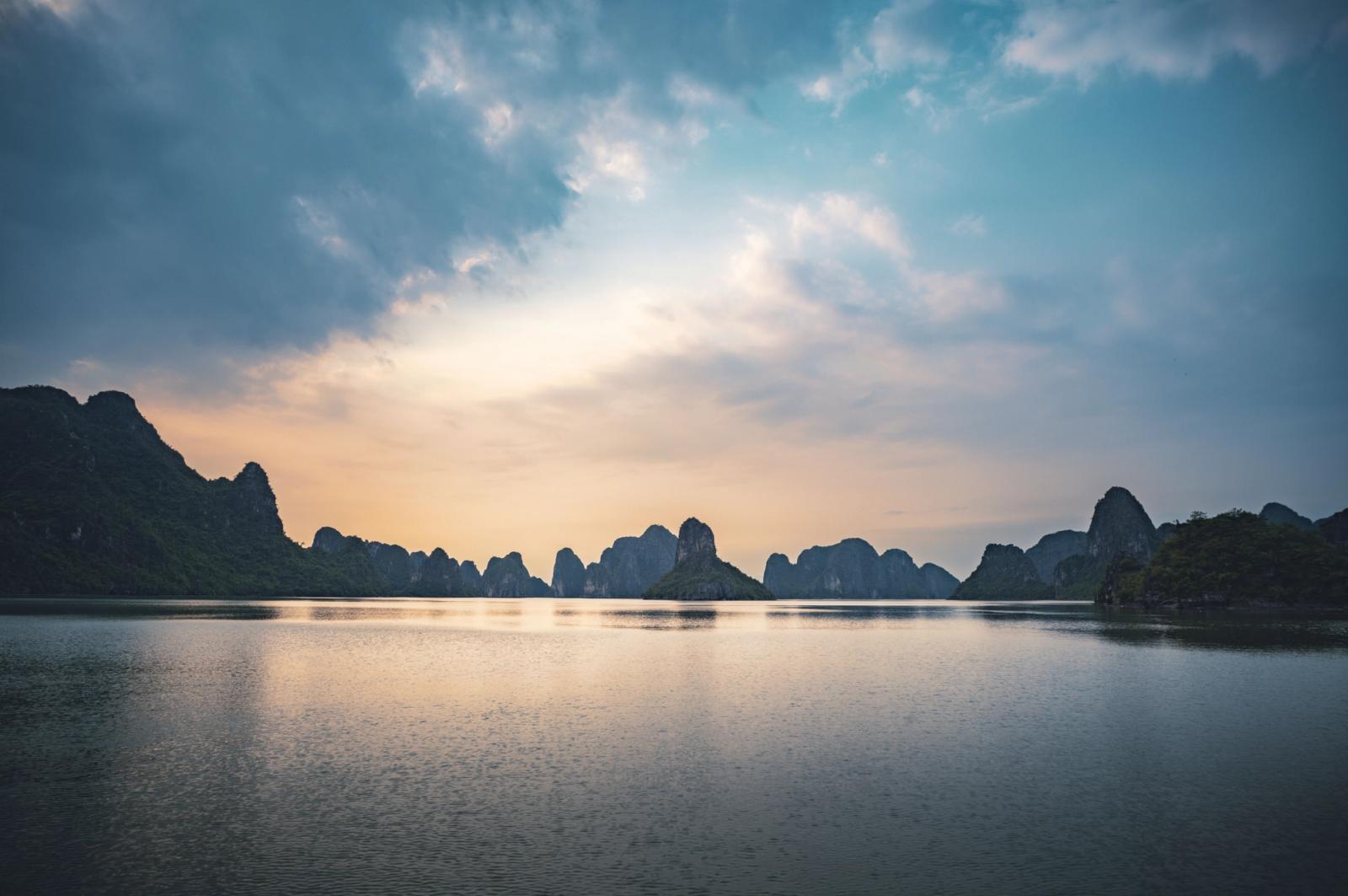 Peaceful view of Halong Bay's karst islands at twilight with calm waters and dramatic clouds