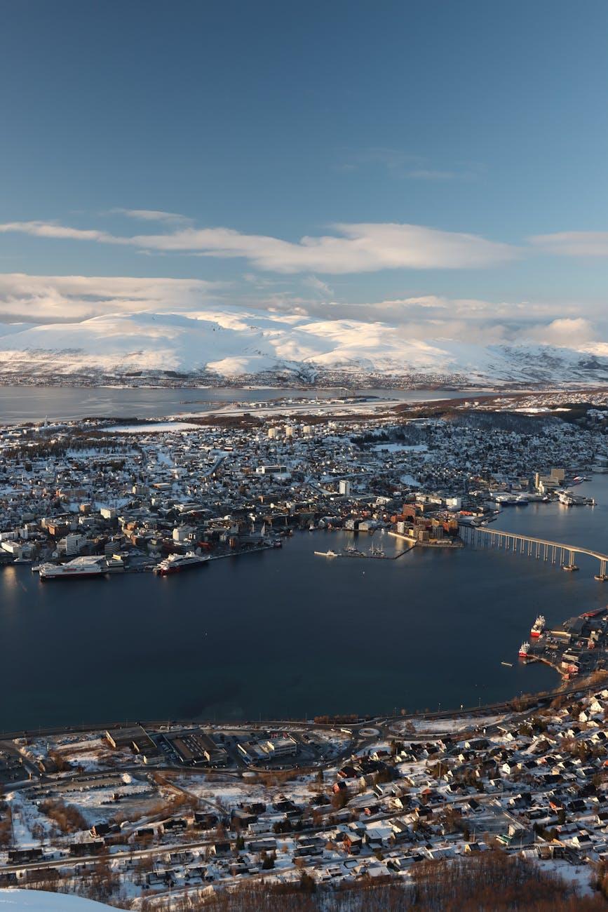 Aerial daylight view of a snowy coastal town on a fjord surrounded by mountains